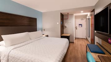 A modern hotel room with a large bed, a TV, a desk, and a bench.