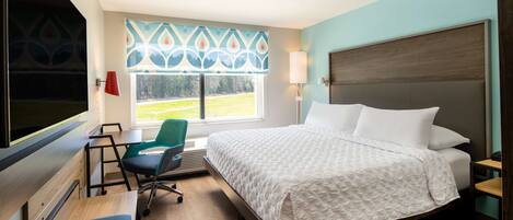 A hotel room with a bed, a desk, a chair, a window with a view, and a TV.