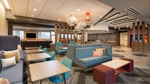 A modern hotel lobby with seating areas, tables, and a kitchen in the background.