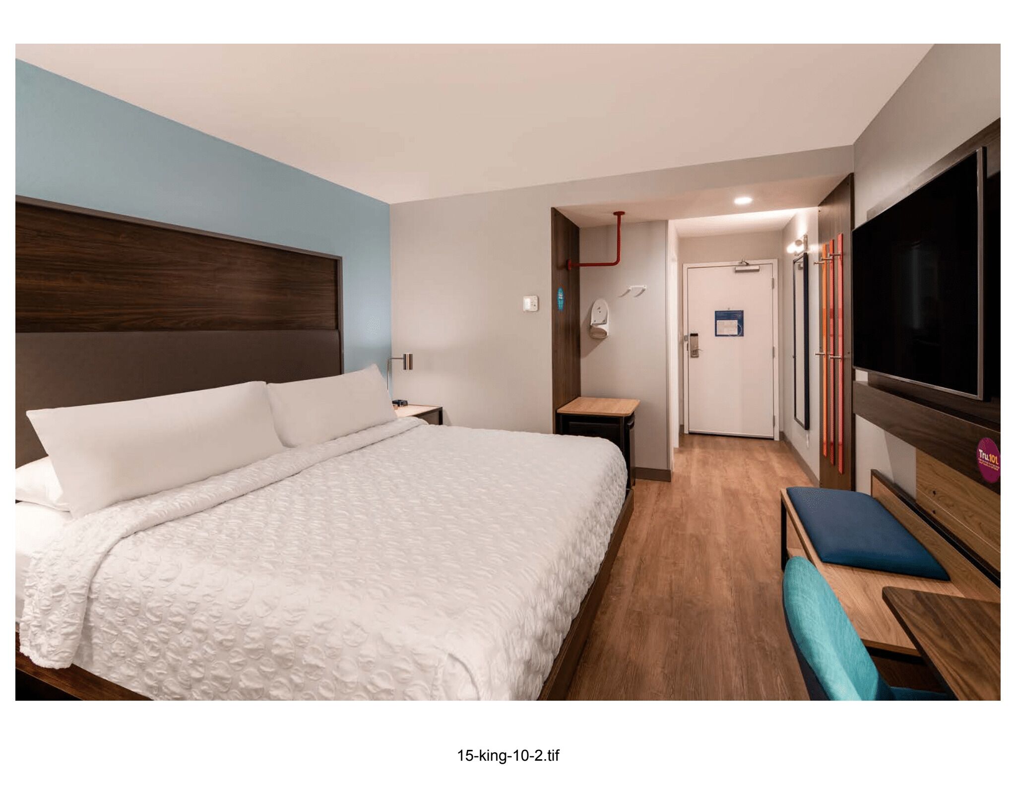 A modern hotel room with a large bed, a TV, a desk, and a bench.