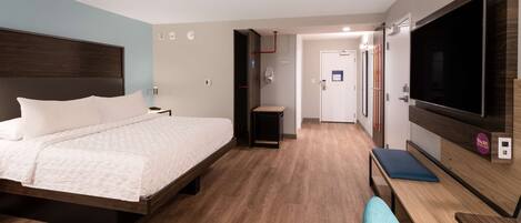 Una habitación de hotel moderna con una cama grande, televisor, escritorio y una silla.