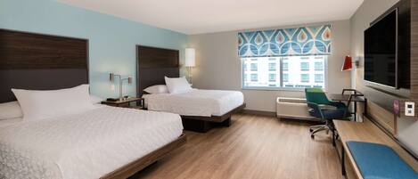 A hotel room with two beds, a desk, a chair, a TV, and a window with a view of buildings.