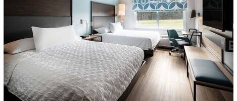 A hotel room with two beds, a desk, a chair, a TV, and a window with a view of the outdoors.