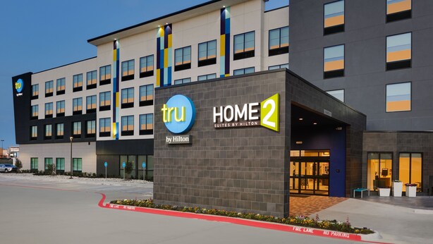 Un moderno edificio de hotel con un letrero que dice "tru HOME 2 by Hilton" y un área de estacionamiento con un letrero de "No Estacionar".