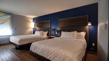 A hotel room with two beds, wooden flooring, and dark blue walls.