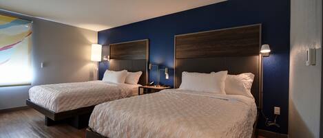 Habitación de hotel con dos camas, suelo de madera y paredes azul oscuro.