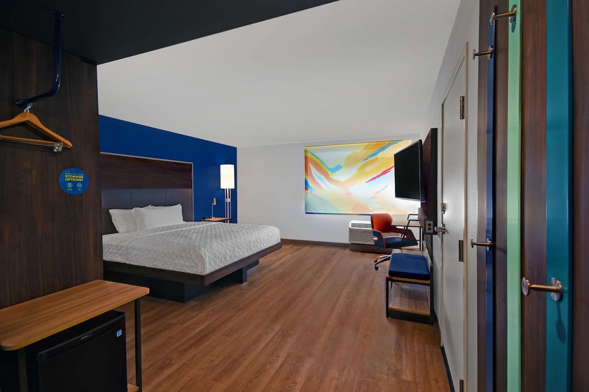 Habitación de hotel moderna con cama, escritorio, silla, televisor y un cuadro abstracto y colorido en la pared.