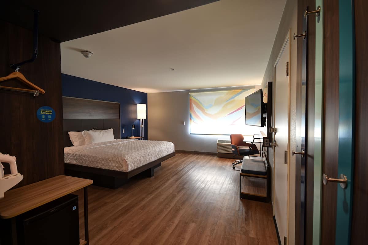 Una habitación de hotel moderna con una cama grande, un escritorio y una silla. Hay una ventana con vista a la ciudad y un televisor montado en la pared.