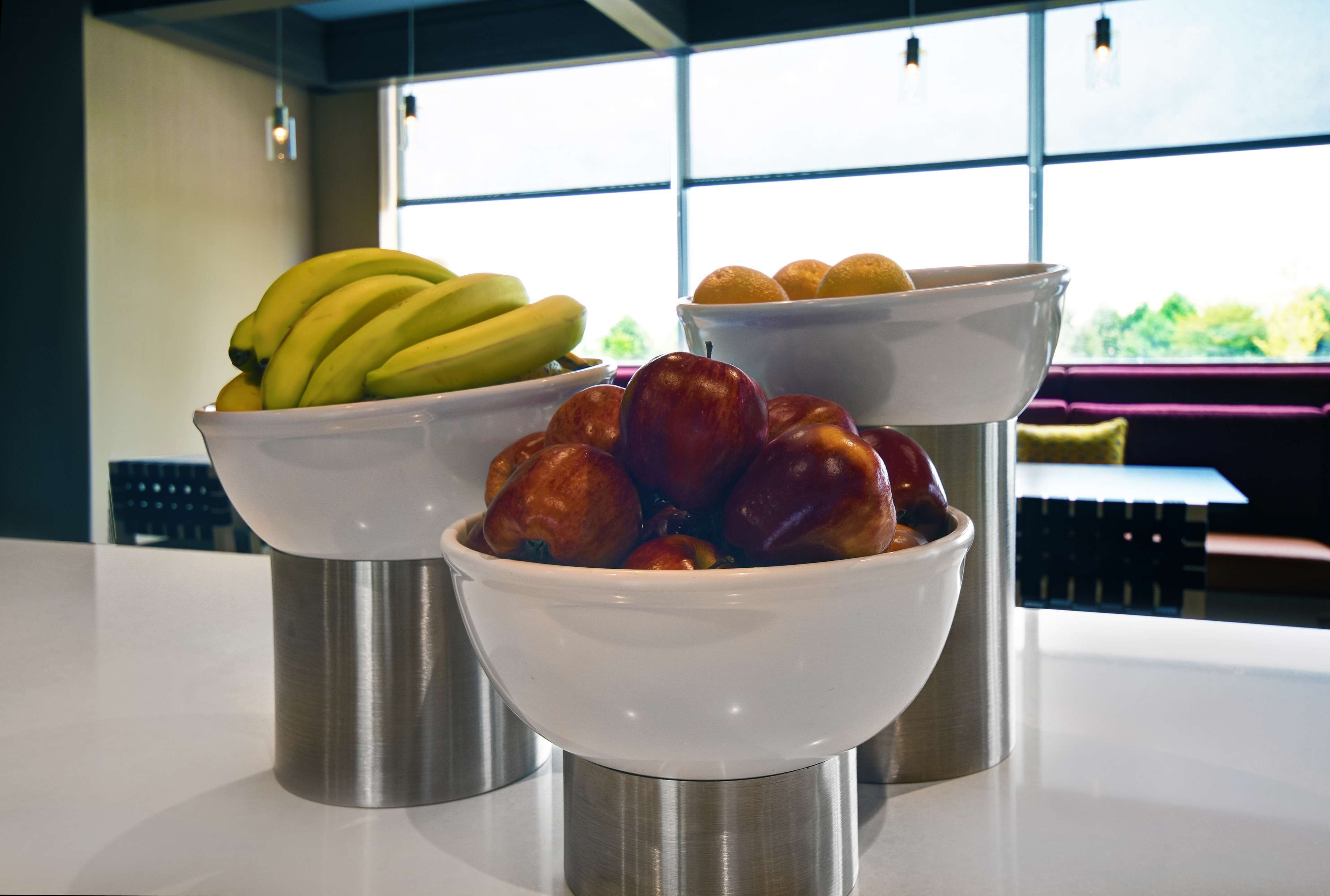 Three white bowls on a stainless steel stand, each containing different fruits.