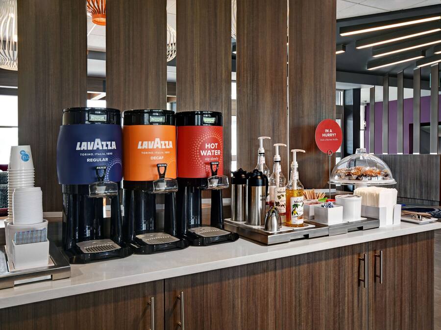 A coffee station with Lavazza espresso machines, a hot water dispenser, and a variety of coffee-related items.
