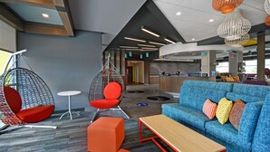Un espace de détente moderne avec un canapé bleu, des fauteuils orange et un fauteuil suspendu.