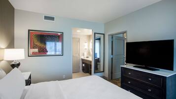 A hotel room with a bed, a TV, a dresser, a lamp, and a painting on the wall.