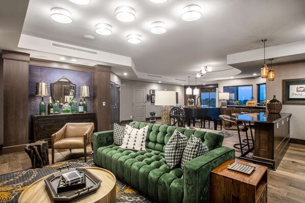 A modern hotel lobby with a green velvet sofa, a wooden coffee table, a bar area, and a dining space. - Homewood Suites by Hilton Salina Downtown (Salina)