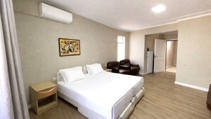 Ein Hotelzimmer mit einem Bett, einem Schreibtisch, einem Stuhl, einem Bild an der Wand und einer Klimaanlage.