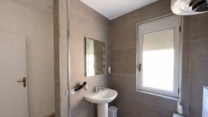 Ein modernes Badezimmer mit einem weißen Waschbecken, einem Spiegel und einem Fenster.