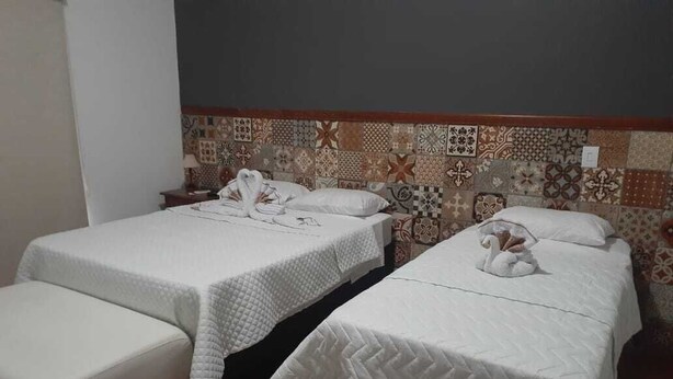 Two single beds with white bedding and towels, a small bench, and a patterned tile wall.
