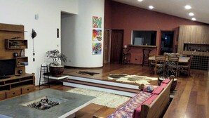 A spacious living room with a large sofa, a coffee table, and a fireplace. There are wooden cabinets and a dining area in the background. - Pousada Vale do Sol (Embu das Artes)