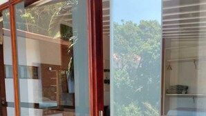 A room with a sliding glass door leading to a balcony with a view of greenery and a building. - Pousada Vale do Sol (Embu das Artes)