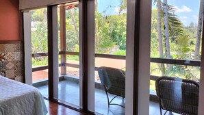 A room with a bed, a chair, and a balcony with a view of greenery. - Pousada Vale do Sol (Embu das Artes)