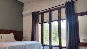 A bedroom with a bed, a window with curtains, an air conditioning unit, and a view of greenery outside. - Pousada Vale do Sol (Embu das Artes)