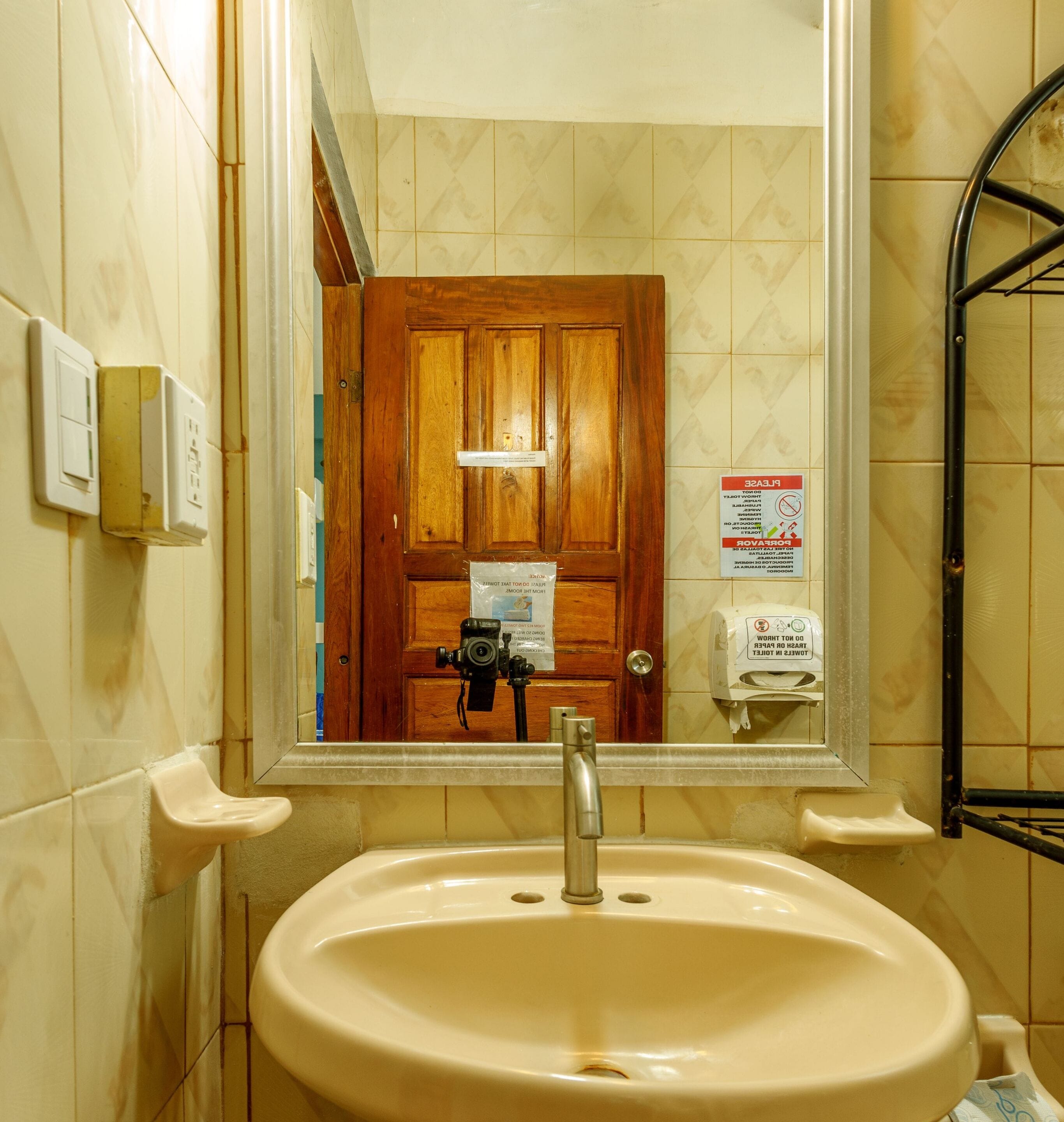 A bathroom with a sink, a wooden door, a mirror, and a hand dryer.