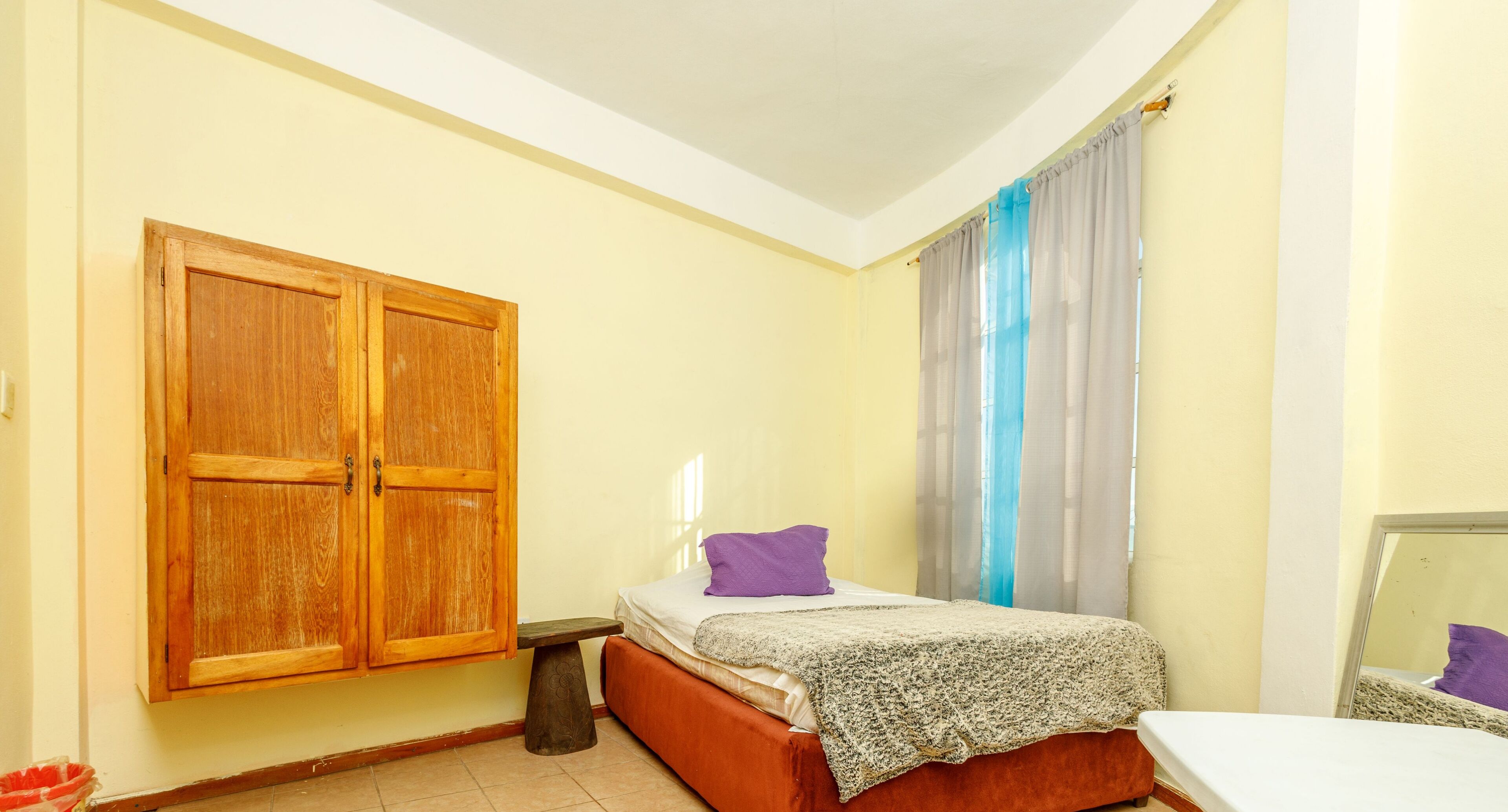 Un dormitorio con cama, armario de madera, mesita de noche pequeña y ventana con cortinas.