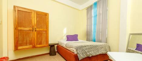 Un dormitorio con cama, armario de madera, mesita de noche pequeña y ventana con cortinas.