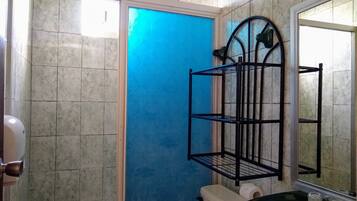 Une salle de bain avec des toilettes, un lavabo et un miroir. Il y a une porte bleue et une étagère en métal noir.