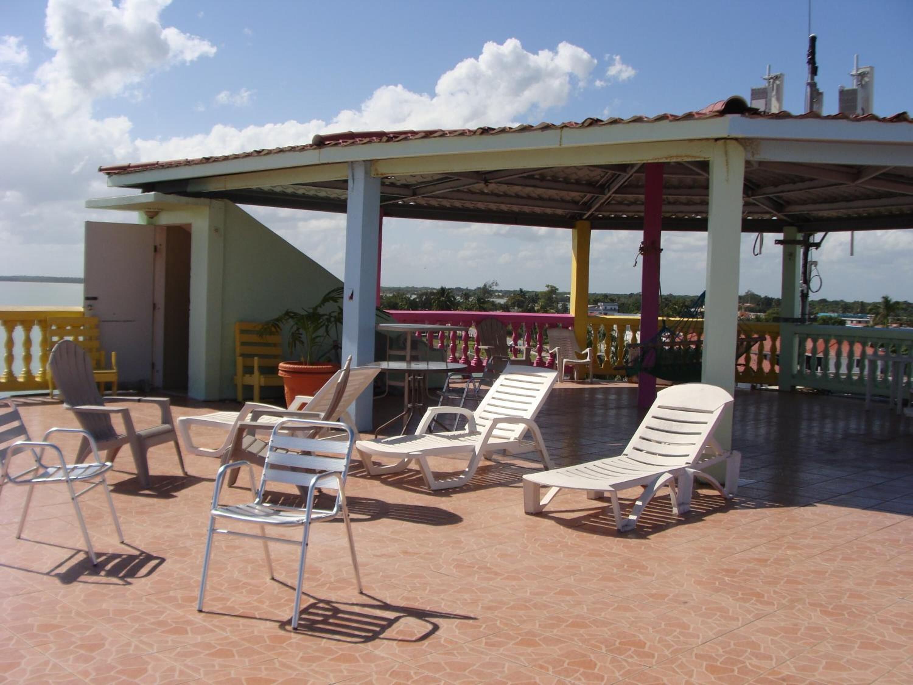 A covered outdoor seating area with lounge chairs and a table, overlooking a scenic view.