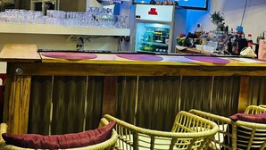 A bar area with wicker chairs, a neon sign, a TV screen, and a shelf with bottles. - Mirador Hotel (Corozal)