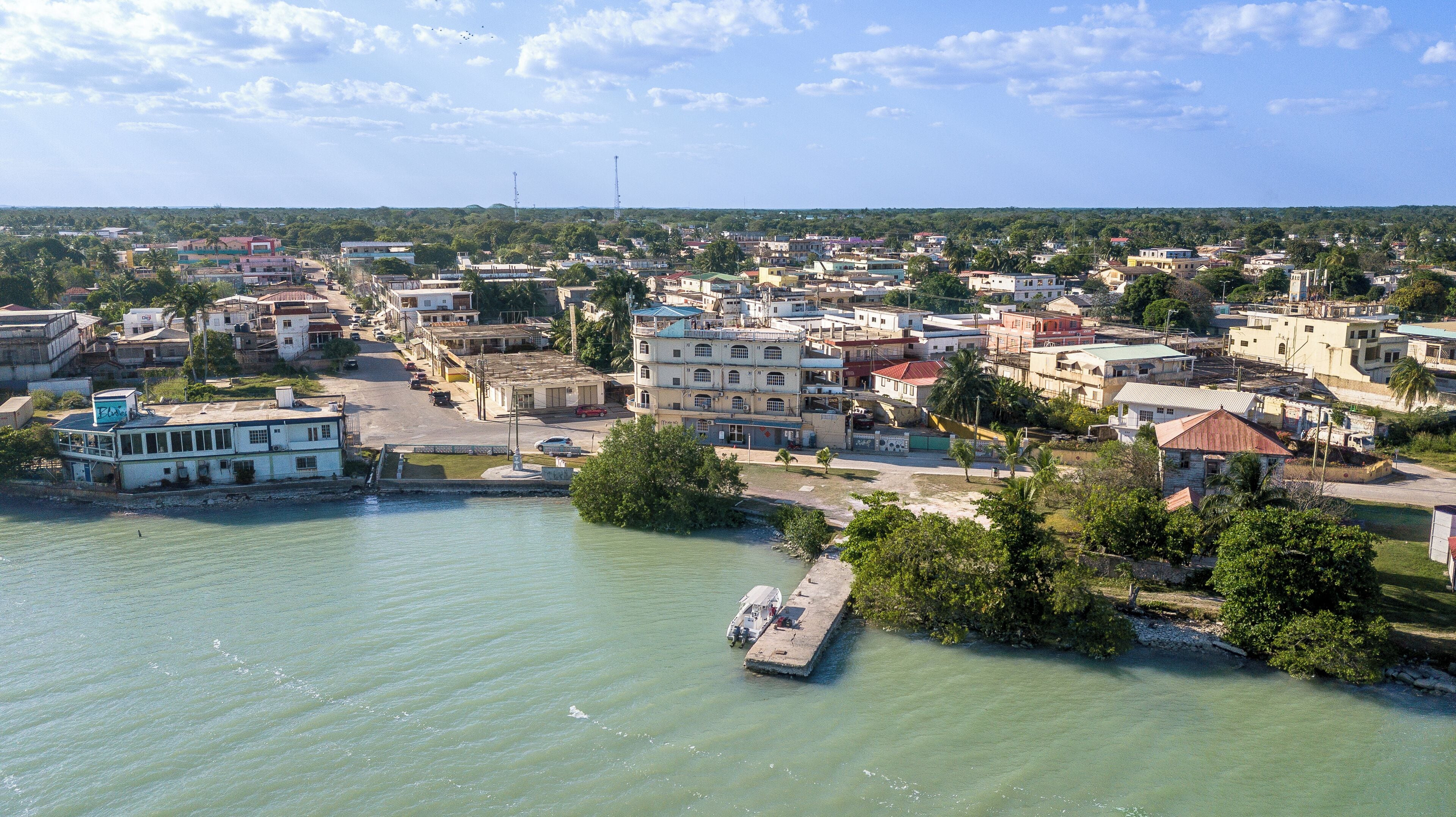 A coastal town with buildings along the waterfront, a dock with a boat, and a clear sky.