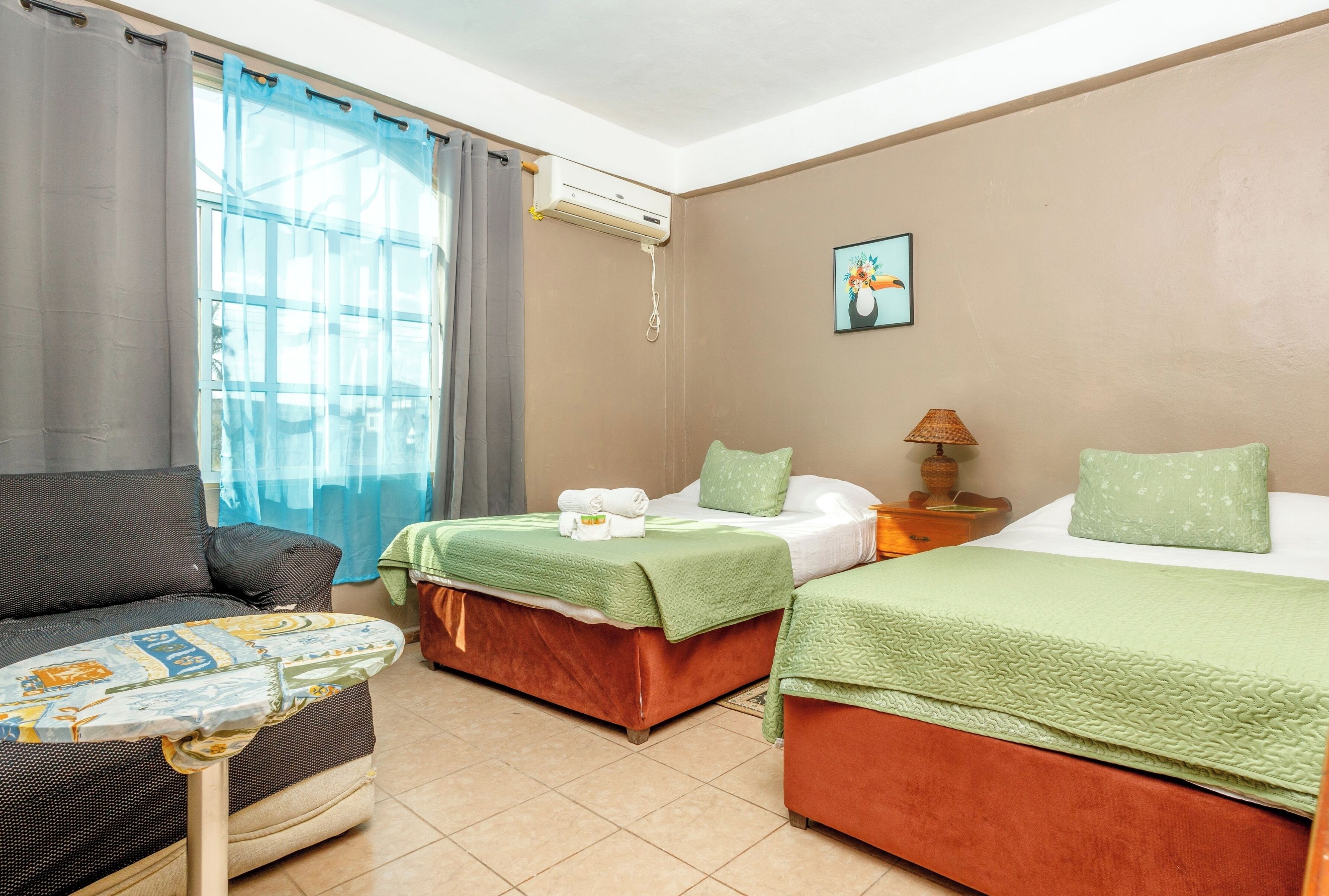 A hotel room with two beds, a sofa, an air conditioning unit, and a painting on the wall.