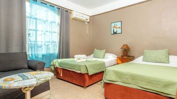 A hotel room with two beds, a sofa, an air conditioning unit, and a painting on the wall.