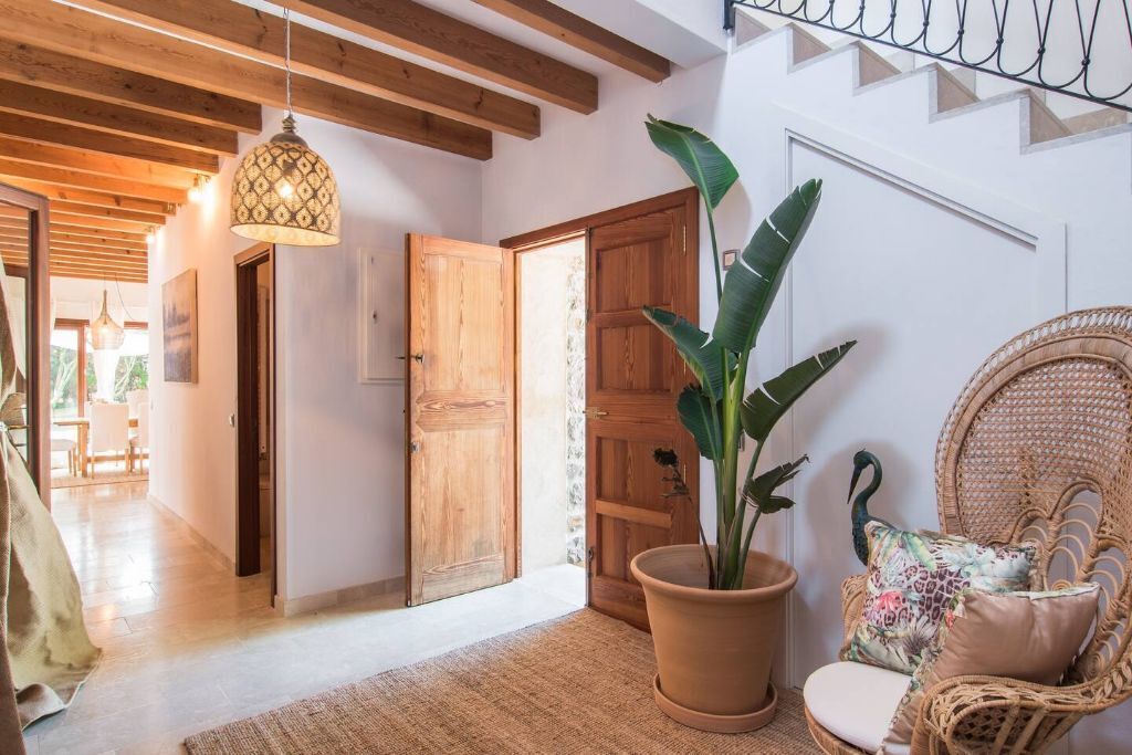 A cozy room with a wooden door, a large potted plant, a wicker chair with a cushion, and a hanging light fixture.