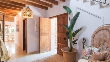 A cozy room with a wooden door, a large potted plant, a wicker chair with a cushion, and a hanging light fixture.