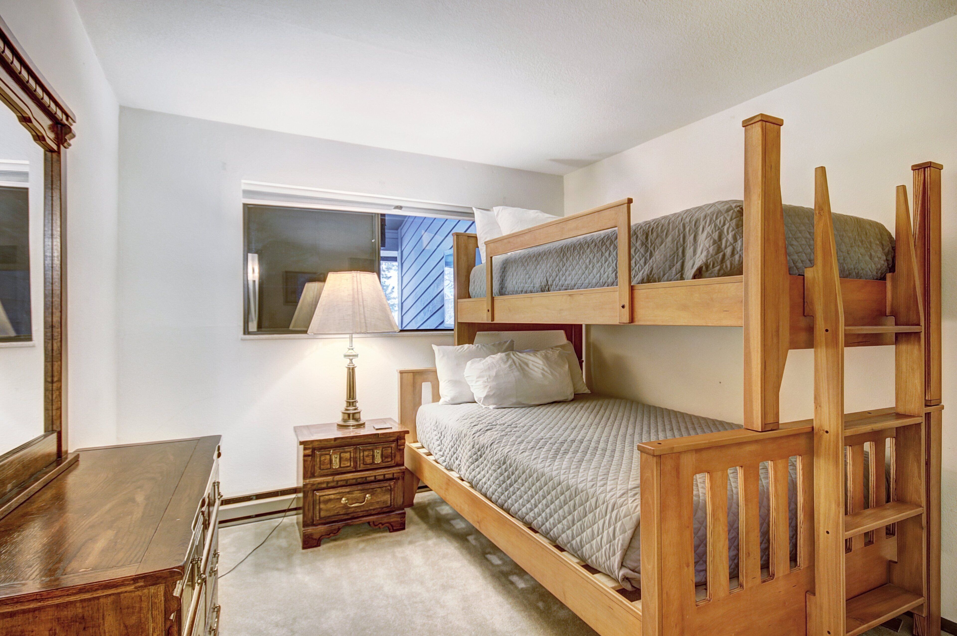 Una cama litera con cabecera de madera, una mesita de noche con lámpara y un espejo en la pared.