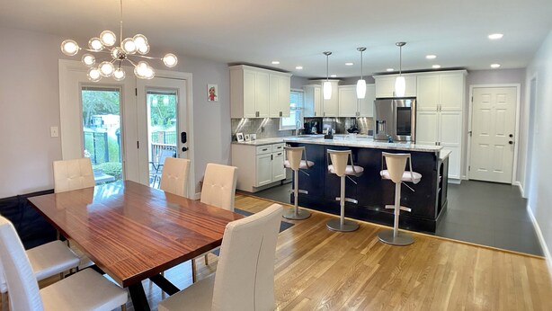 A modern kitchen with white cabinets, a central island with bar stools, and a dining area with a wooden table and chairs. - PRIVATE heated pool & hot tub, dogs ok, near Keeneland (Lexington)