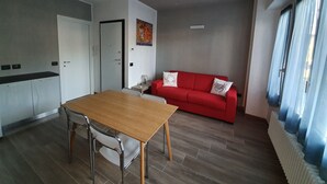 En moderne stue med en rød sofa, et træspisebord og et køkken med skabe.