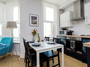 Une cuisine moderne avec des meubles blancs, un four à micro-ondes et une cuisinière. On y trouve une table à manger avec des chaises et un vase rempli de fleurs.