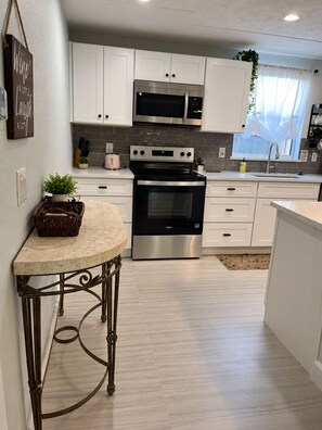 A modern kitchen with white cabinetry, stainless steel appliances, and a marble countertop.
