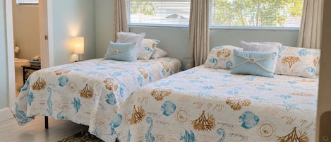 Une chambre avec deux lits, chacun agrémenté de la même literie et des mêmes oreillers, une fenêtre avec des rideaux, une lampe et un tapis à motifs.