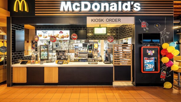 A McDonald's kiosk with a kiosk order sign, menu display, and a digital ordering screen.