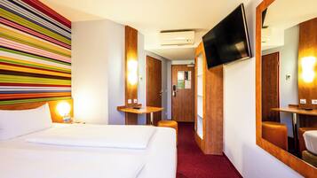 A hotel room with a large bed, a TV mounted on the wall, a wooden desk, and a mirror.