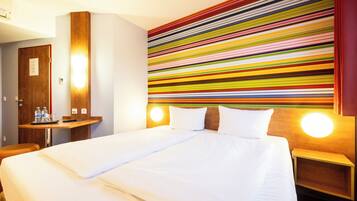 Une chambre d’hôtel avec un grand lit, une table de chevet en bois, un bureau avec une chaise et un mur rayé aux couleurs vives.