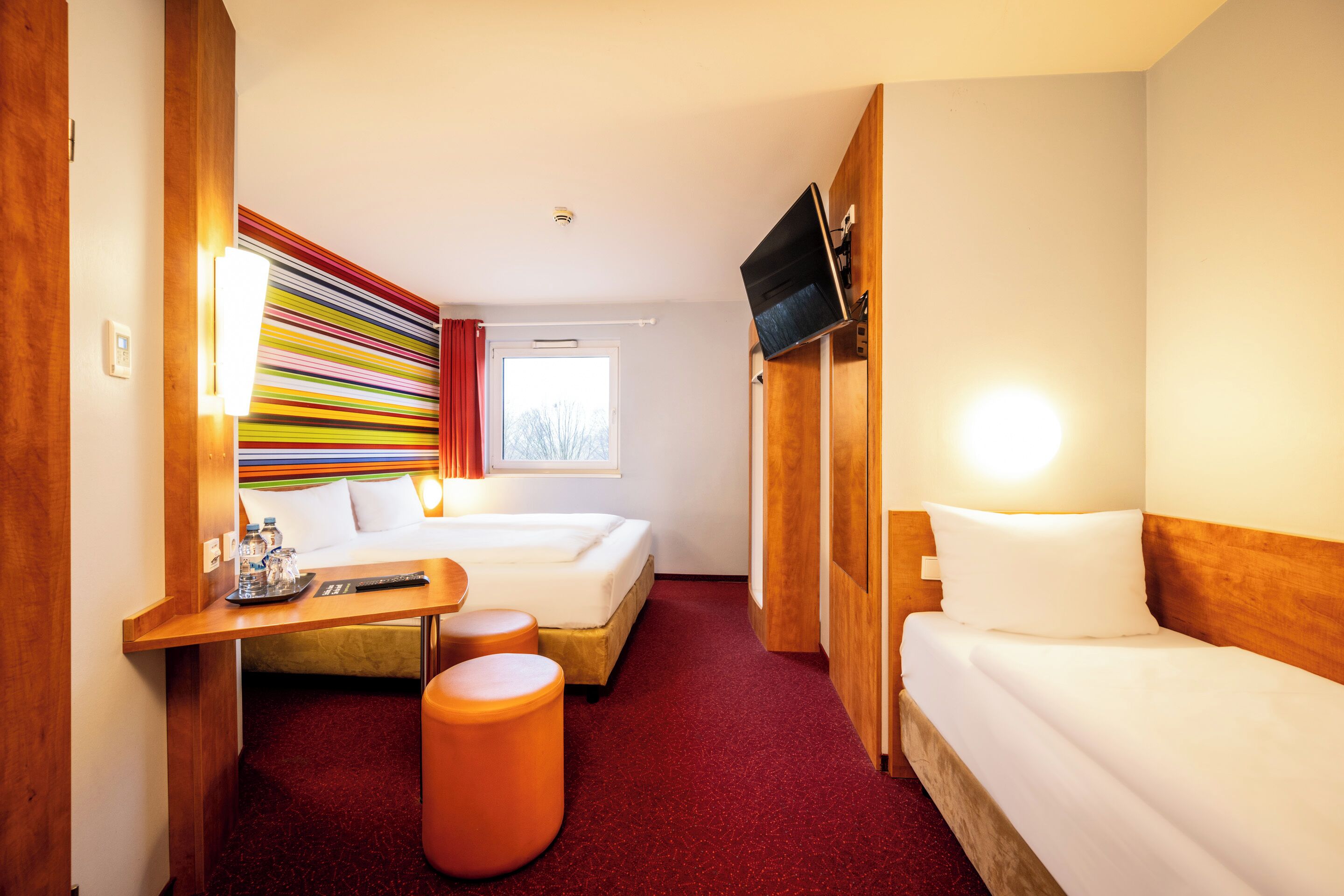 A hotel room with a bed, a desk, a TV, and a window.