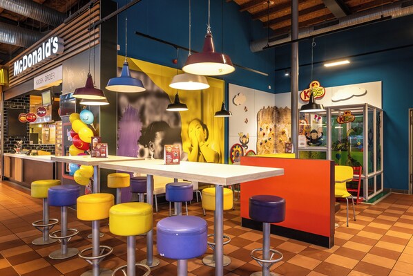 A colorful indoor space with a McDonald's kiosk, yellow and purple stools, and a children's play area.