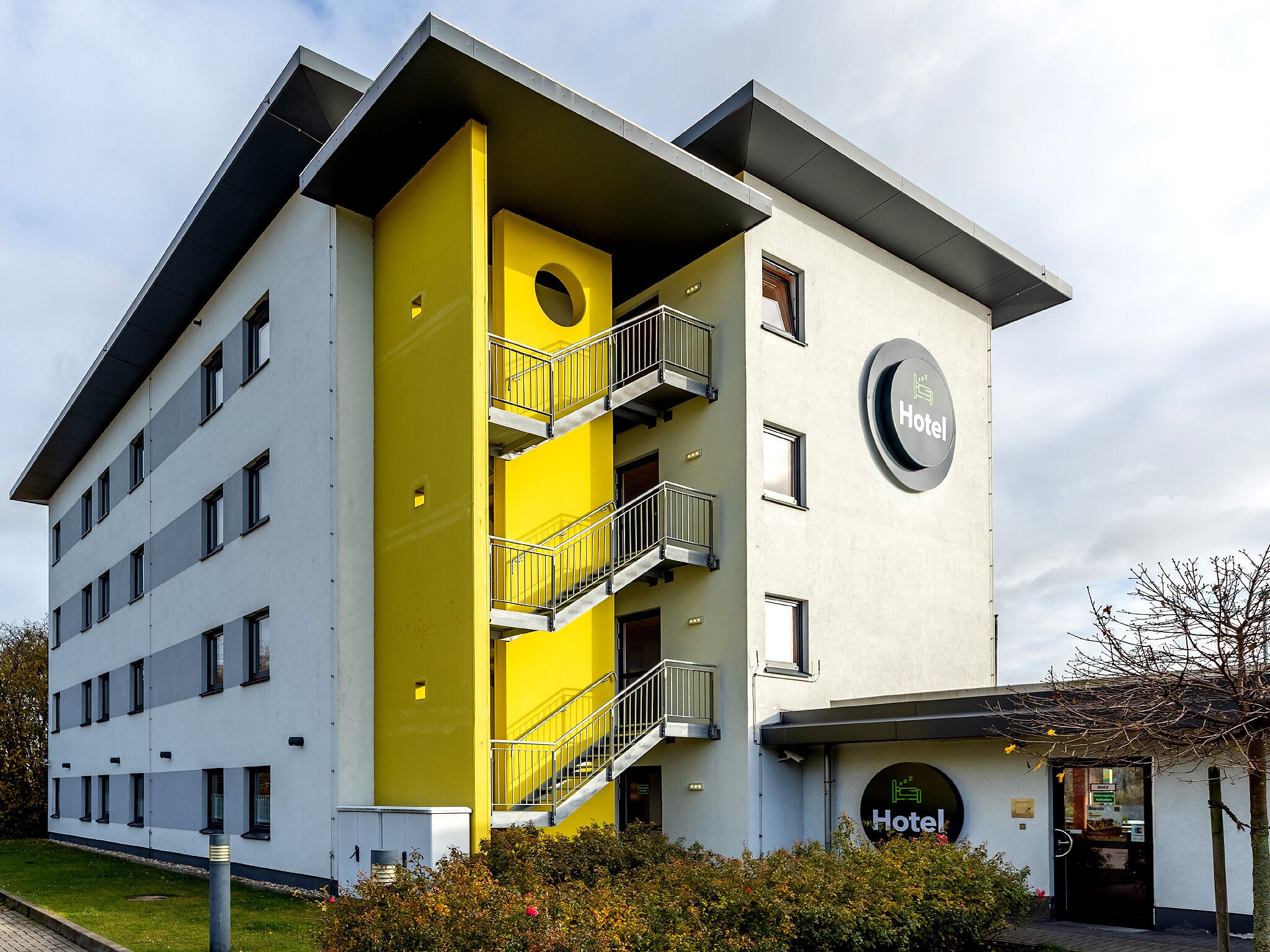 Un moderno edificio de hotel con fachada amarilla y gris, varios balcones y una entrada visible.