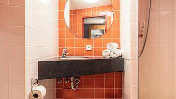 Une salle de bain avec des toilettes blanches, un lavabo avec un miroir au-dessus et un espace douche.