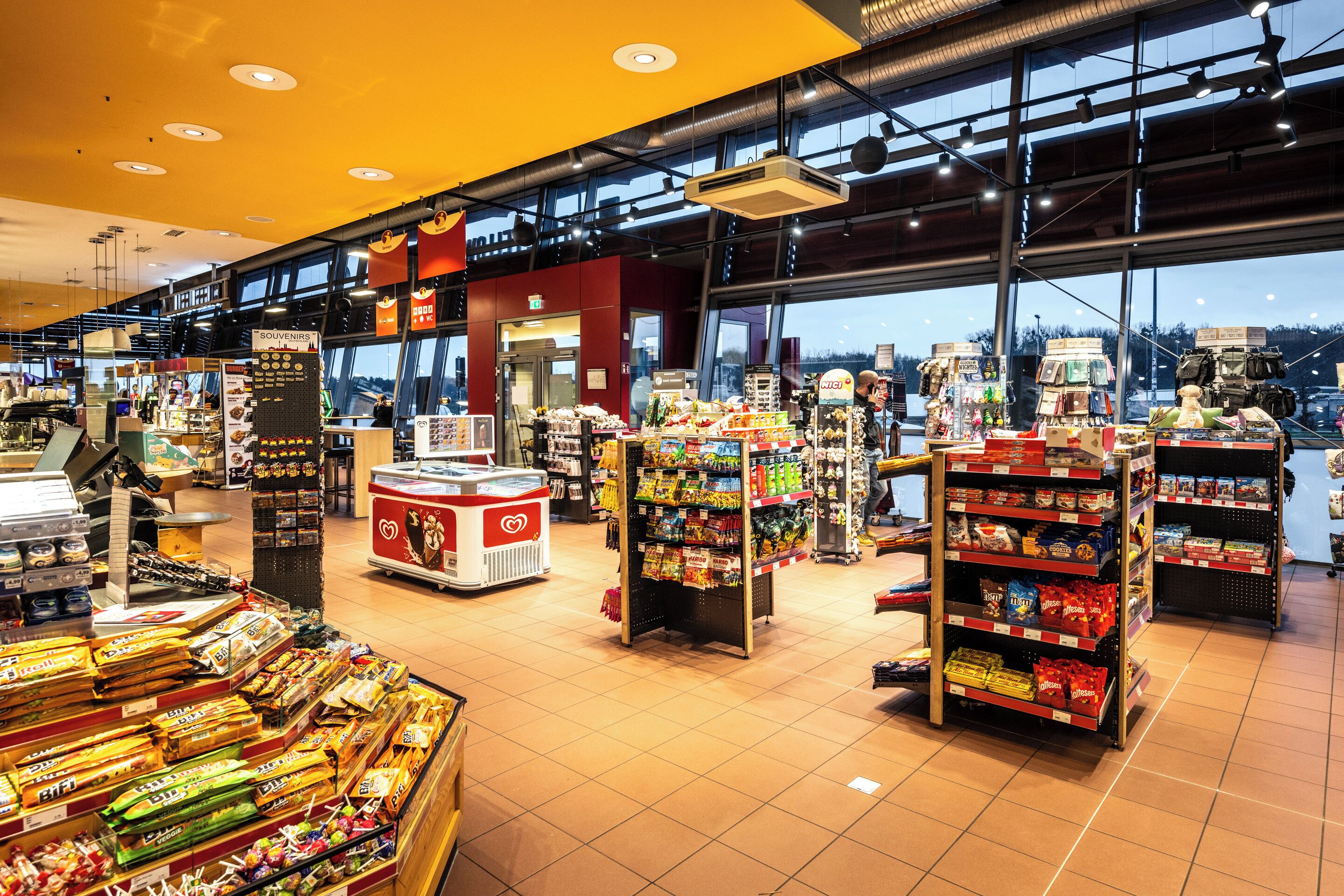 A spacious supermarket interior with wide aisles, refrigerated sections, and a variety of packaged goods on shelves.