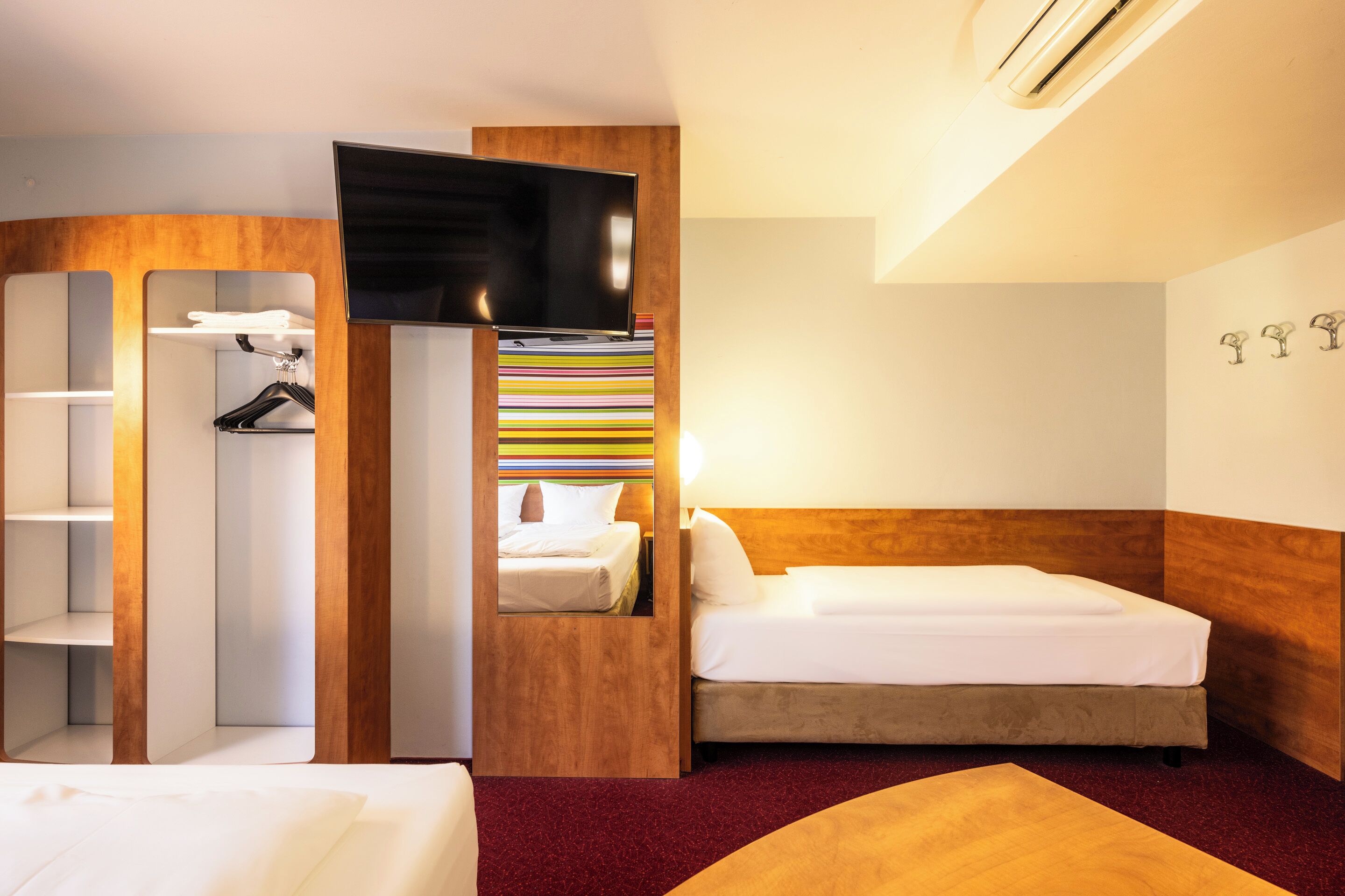 A hotel room with a bed, a desk, a wardrobe, and a TV.